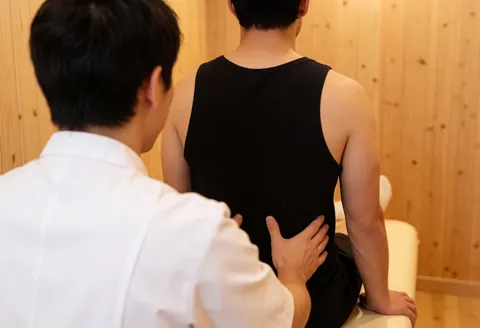 Professional osteopath treating a seated patient's back in a calm clinic with light wood walls and warm lighting