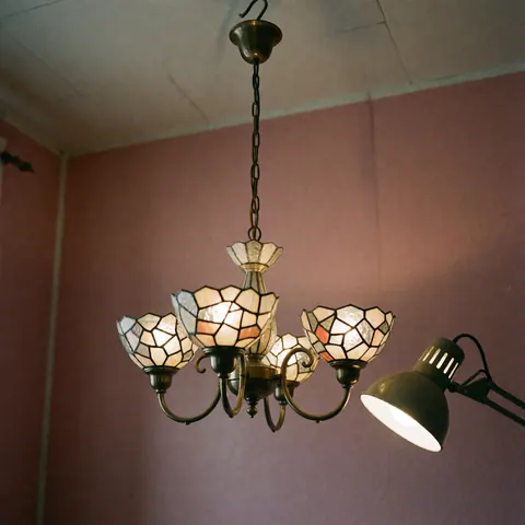 Crystal chandelier with geometric patterns illuminated by a work lamp hanging on a pink wall in a craft workshop