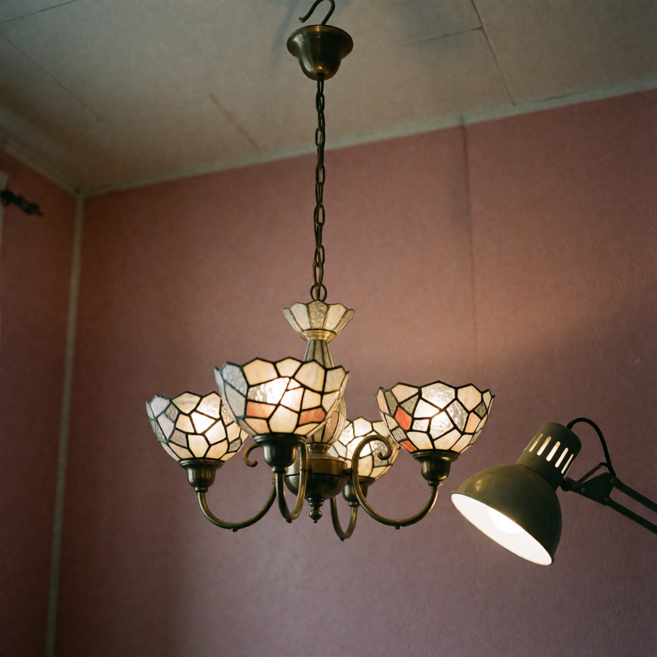 Crystal chandelier with geometric patterns illuminated by a work lamp hanging on a pink wall in a craft workshop