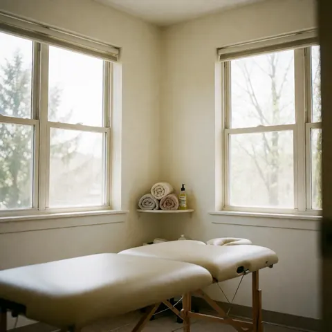 Bright and clean osteopathy treatment room featuring therapy beds, natural light from windows, and stacked towels for patient comfort.
