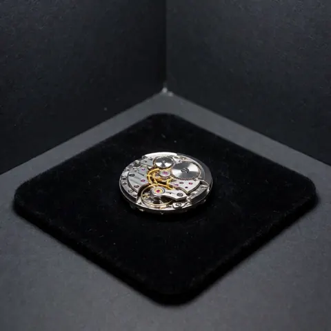 Close-up view of an open Swiss watch movement mechanism resting on a black velvet surface with soft lighting against a gray background