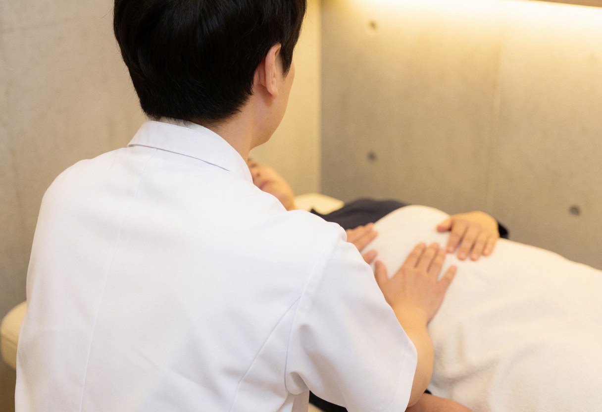 Osteopath in white coat performing visceral adjustment on patient lying on treatment bed in calm professional clinic setting