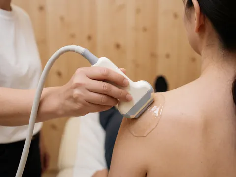 Close-up of an ultrasound transducer applying gel to a patient's shoulder for advanced physiotherapy treatment on a wooden surface