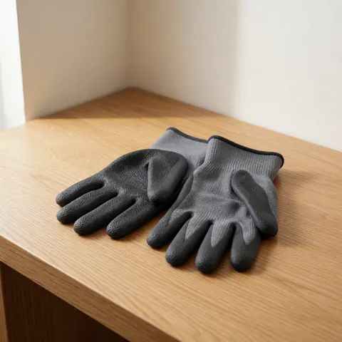 Durable charcoal gray work gloves with textured grip and knuckle reinforcement resting on a light wooden surface under natural light.