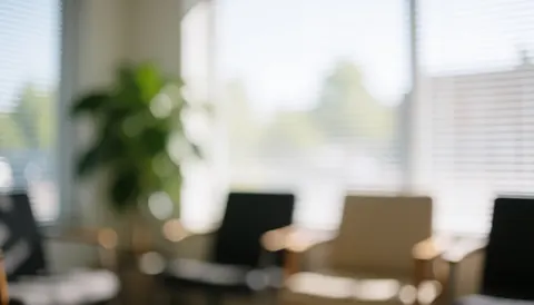 A blurred background of a quiet waiting area featuring chairs, plants, and windows with natural light, suitable for text overlay