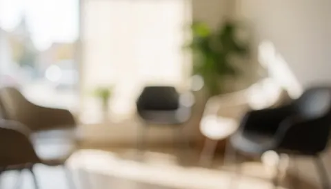 A softly blurred interior shot of a quiet waiting area featuring a chair and a potted plant, creating a calm and professional atmosphere suitable for text overlay.