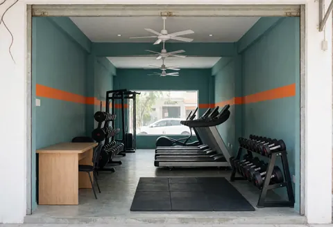 Small gym interior featuring teal walls, gray flooring, and visible cardio and weight machines near a clean entrance.