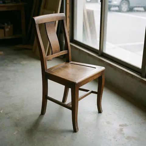 A beautifully restored wooden chair with polished finish, positioned in a workshop setting with natural light from a window, showcasing quality furniture repair results.