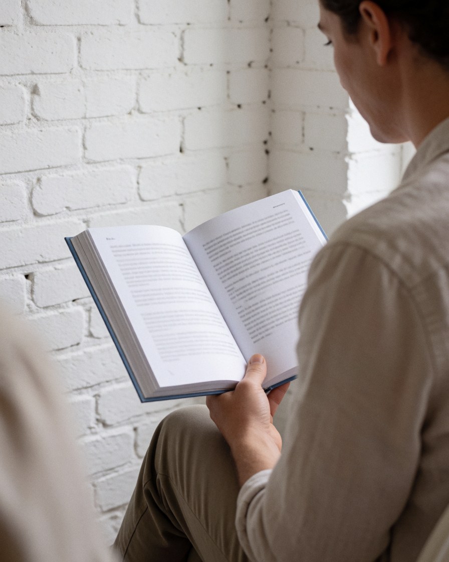 A serene adult reading an open book in a calm indoor setting with natural light and a brick wall background