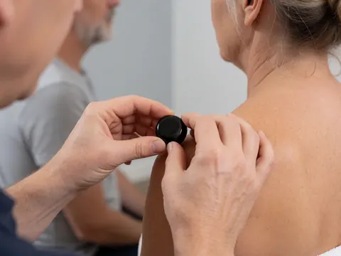 Close-up of a therapist's hands placing a black obsidian stone on a client's shoulder during a reiki session with soft lighting and a blurred background