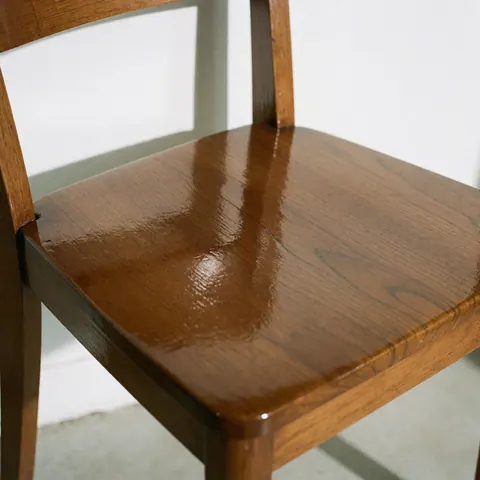 A close-up view of a restored wooden chair with a glossy varnished finish, highlighting the wood grain and furniture repair details.