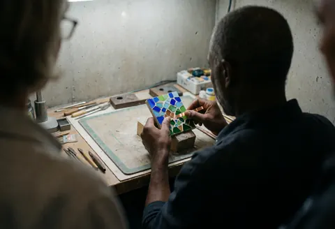 Back view of artisan working on decorative marble panel with copper in workshop with concrete walls and tools