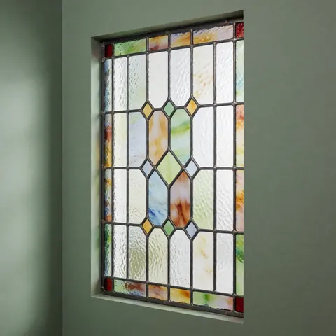 A close-up view of a restored decorative stained glass window featuring green tones and intricate patterns set in a wooden frame, highlighting the craftsmanship of the decorative glasswork.