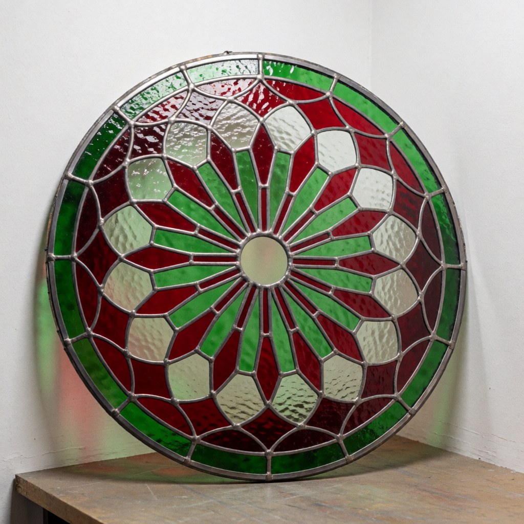 Detailed view of a completed decorative glass oculus featuring radial red and green patterns set in a metal frame against a white wall