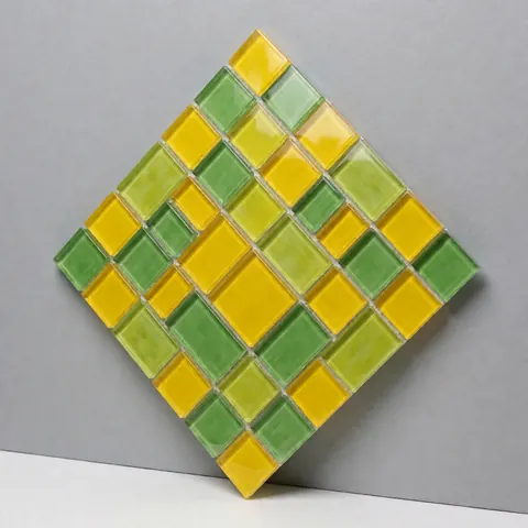 Decorative mosaic panel featuring yellow and green glass pieces in a geometric pattern, displayed against a neutral gray wall for kitchen or bathroom design.