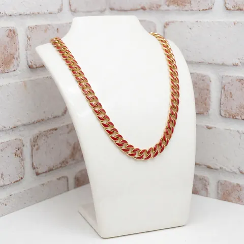 Gold necklace featuring bright red enamel displayed on a white stand against a painted brick wall, suitable for jewelry store product catalogs.