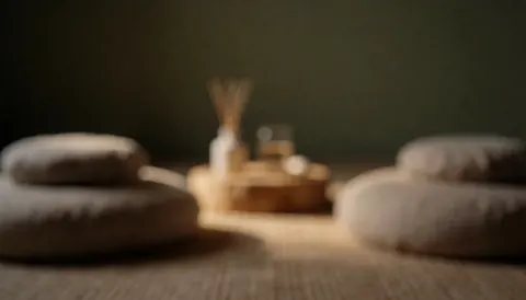 Softly lit zen room background featuring earth-toned meditation cushions, an essential oil diffuser, and warm wooden textures for a calm atmosphere