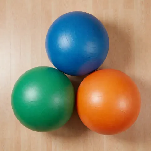 Several colorful swiss exercise balls in blue green and orange arranged on a clean wooden floor for advanced physiotherapy and rehabilitation