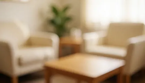 Beige armchairs and wooden table in a warm, calm osteopathy waiting room with a plant and soft lighting.