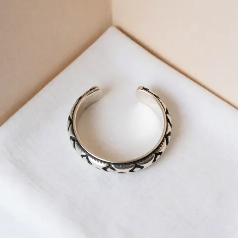 Oxidized silver bracelet with visible artisanal details on white fabric and beige wall with soft lighting