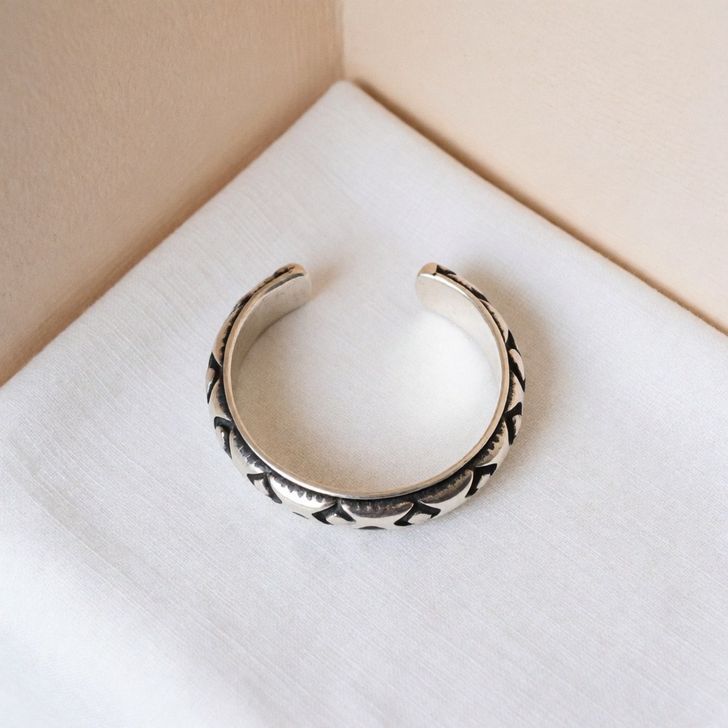 Oxidized silver bracelet with visible artisanal details on white fabric and beige wall with soft lighting