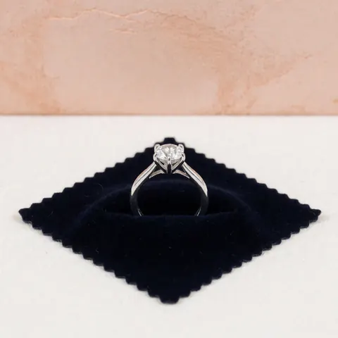 Close-up of a reinforced prong setting on a diamond ring displayed on a black velvet surface with terracotta background