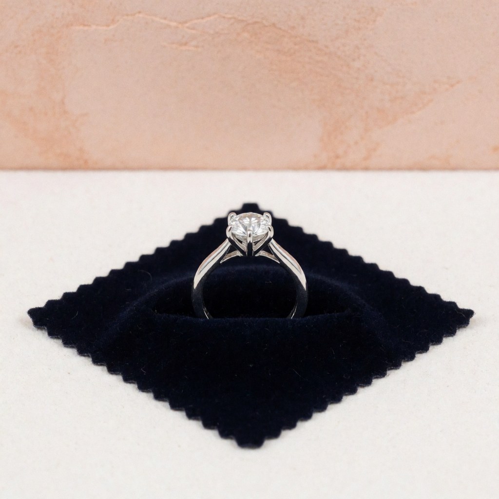 Close-up of a reinforced prong setting on a diamond ring displayed on a black velvet surface with terracotta background