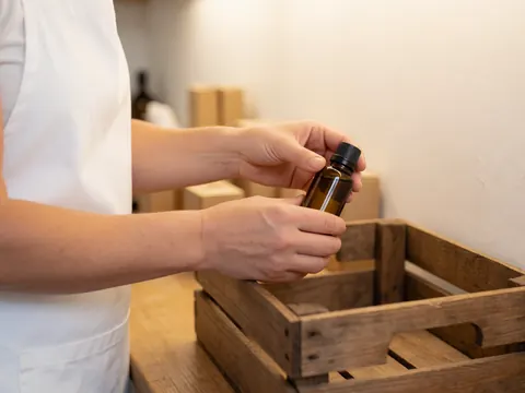 Close-up of hands carefully packing glass essential oil bottles into a wooden box for aromatherapy products