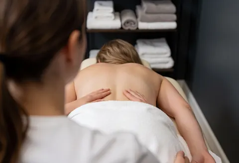Therapist performing chiropractic massage on a client's back on a table with towels in the background