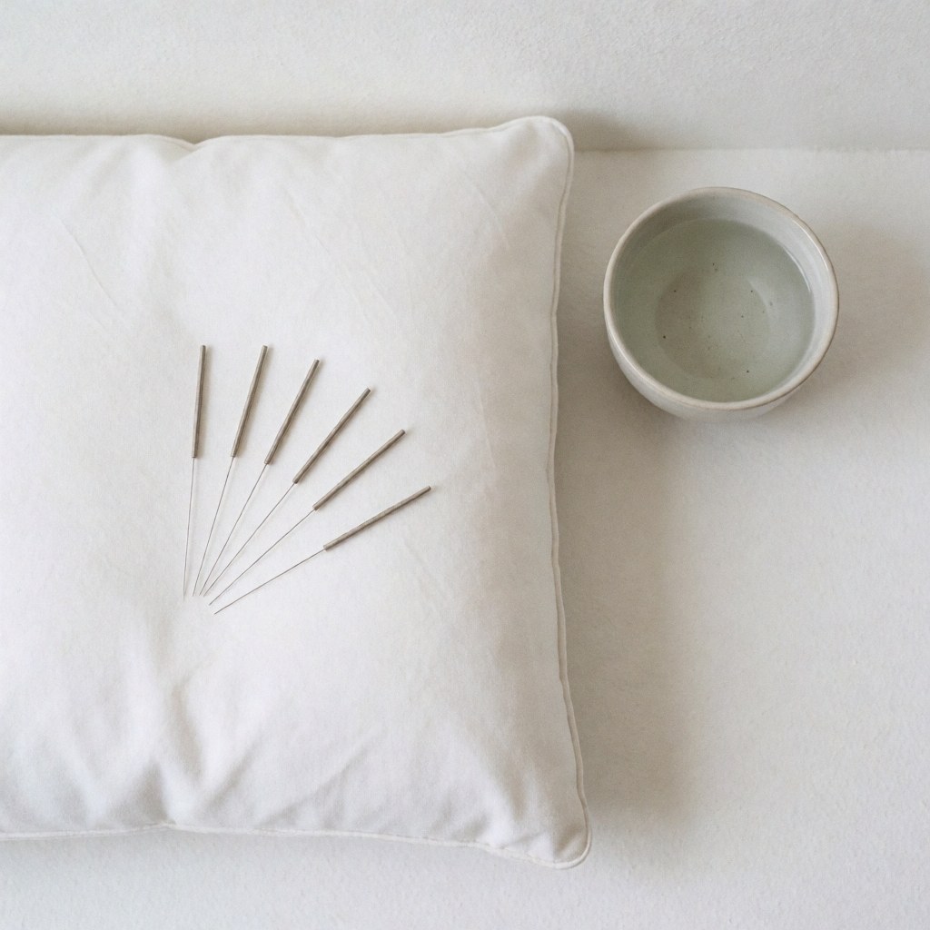 Close-up view of acupuncture needles, a small bowl of water, and meditation cushions arranged neatly on a clean white surface for therapy and wellness