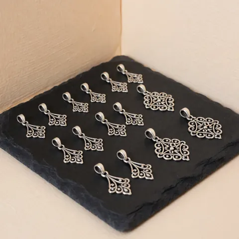 Close-up of oxidized silver filigree charms resting on a black stone surface with a soft beige background, showcasing intricate jewelry repair details.