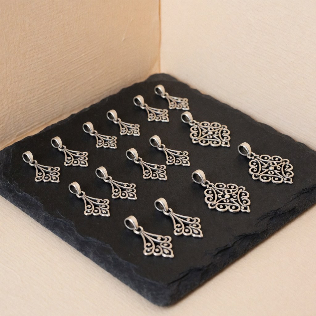Close-up of oxidized silver filigree charms resting on a black stone surface with a soft beige background, showcasing intricate jewelry repair details.
