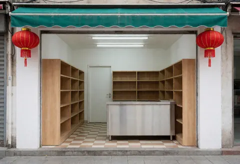 Minimarket entrance featuring white walls, checkered floor, wooden shelves, stainless steel counter, red hanging lanterns, and a green awning.