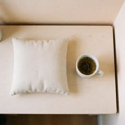 A cozy arrangement featuring a soft cushion, a ceramic tea cup, and wooden table elements to promote relaxation and tranquility for maternal care.