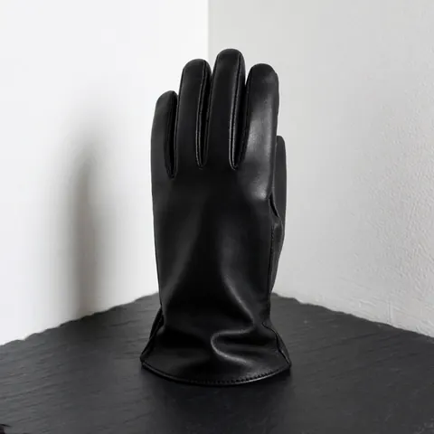 A high-quality black leather glove resting on a dark slate surface with a white wall background and soft lighting highlighting the texture.