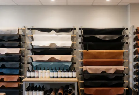 Neatly arranged leather rolls in various colors and dye bottles in a professional workshop setting for leather crafting