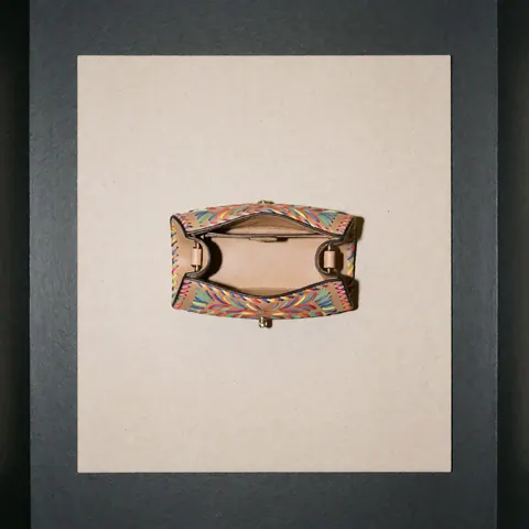Open tan leather handbag featuring colorful embroidery and metallic hardware, displayed on a neutral beige background with even lighting for catalog use