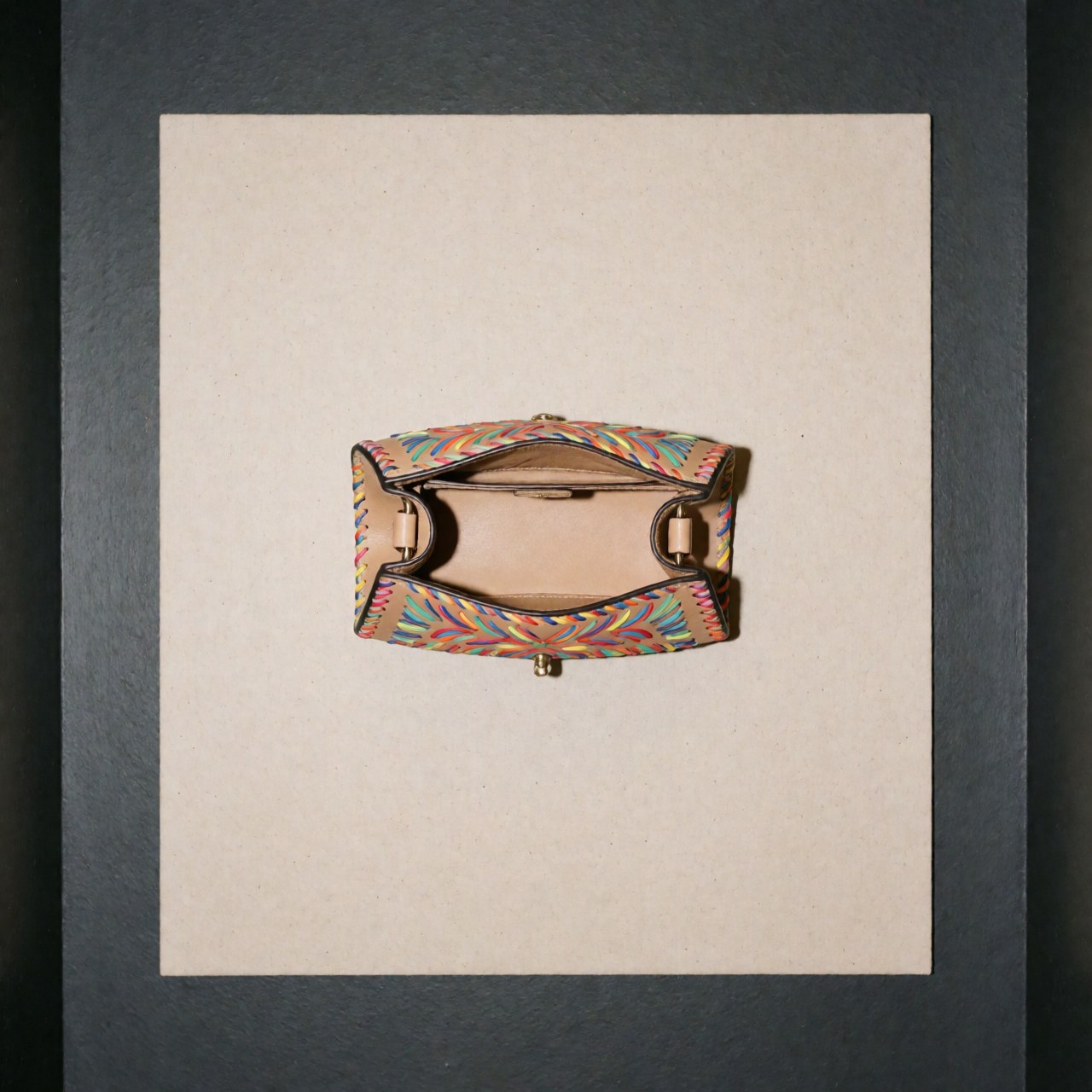 Open tan leather handbag featuring colorful embroidery and metallic hardware, displayed on a neutral beige background with even lighting for catalog use
