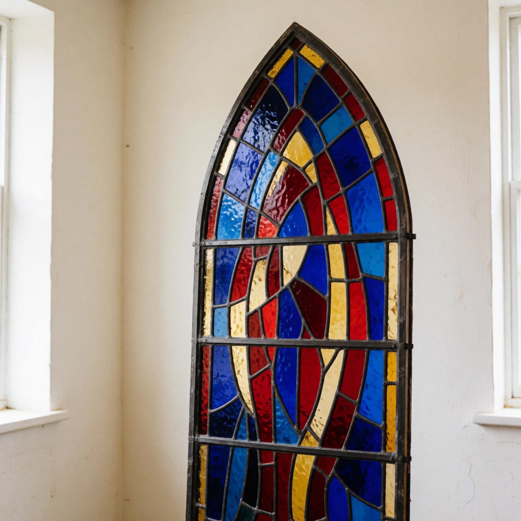 Gothic stained glass window with blue, red, and gold glass mounted in a workshop with white walls and natural light