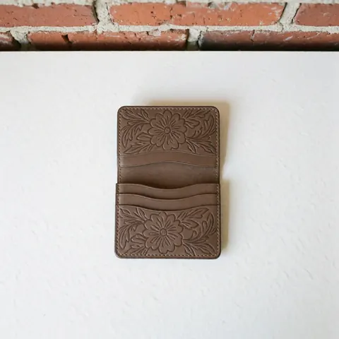 Top view of a brown leather wallet with floral embroidery on a white and red brick background, showcasing clean presentation and visible texture.