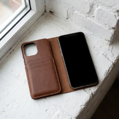 A sleek leather case for a smartphone or credit cards resting on a clean white brick surface, showcasing a minimalist and functional design.