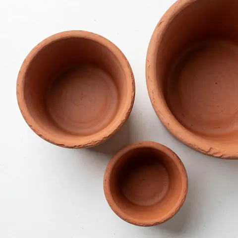 Close-up view of several unglazed terracotta flower pots arranged on a light wooden table, showcasing their natural texture and earthy tones for home decor.