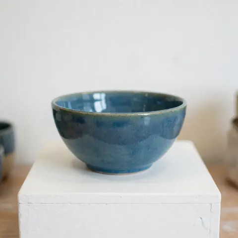 A glossy blue ceramic bowl placed on a white pedestal in a studio setting with soft lighting, ideal for product photography.