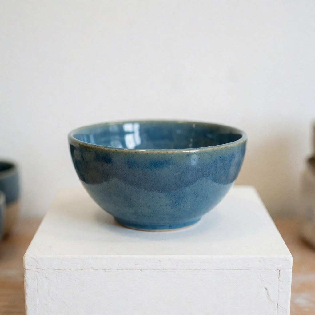 A glossy blue ceramic bowl placed on a white pedestal in a studio setting with soft lighting, ideal for product photography.