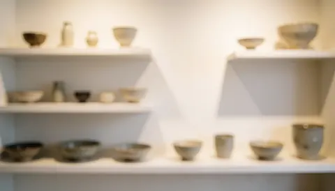 A clean ceramic display cabinet with glass shelves holding handmade pottery, mugs, and vases, serving as a neutral background for business use