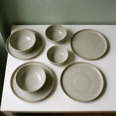 A minimalist ceramic dinnerware set in earth tones, featuring handmade plates and bowls with a natural, elegant finish suitable for modern dining.
