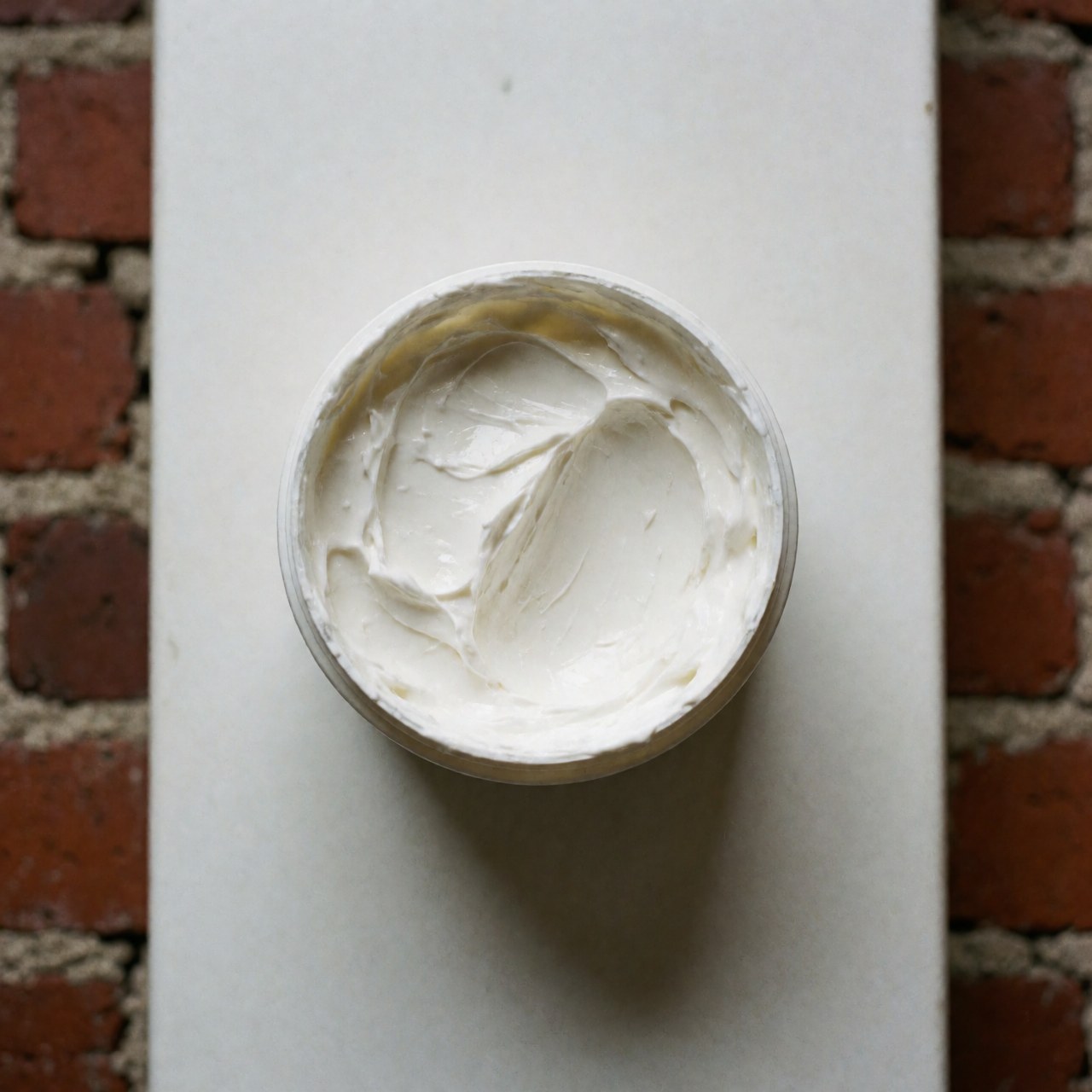 Open tube of foot cream viewed from above on a red brick surface with a clean texture suitable for reflexology salons