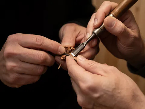Detailed view of wood marquetry carving with chisel and wood shavings on a dark background