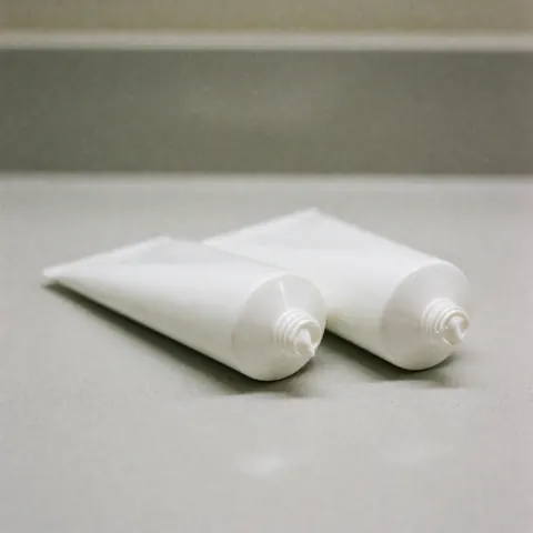 Several tubes of therapeutic cream arranged neatly on a clean white countertop with soft lighting and a blurred background, suitable for osteopathy and post-treatment care products.