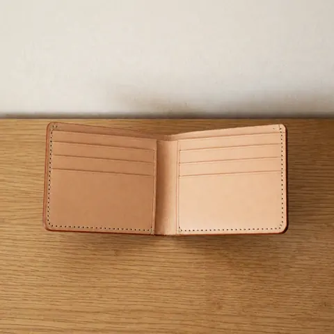 An open brown leather wallet displaying its interior organization and stitching details, resting on a light wooden background